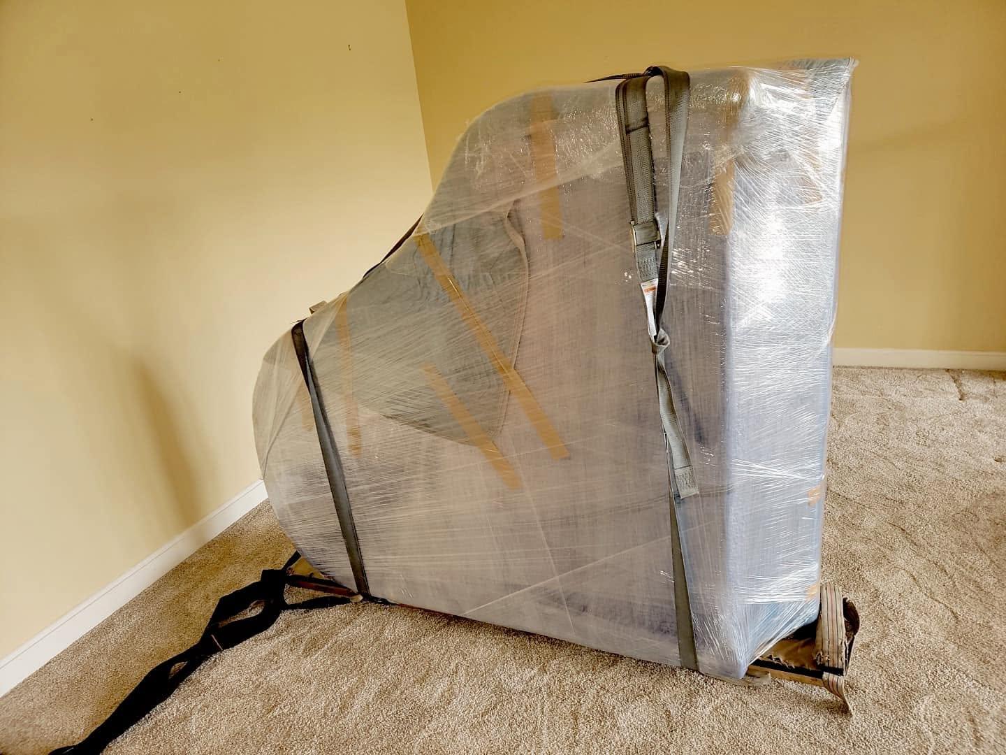 A grand piano wrapped in moving pads and strapped on its side, ready to move
