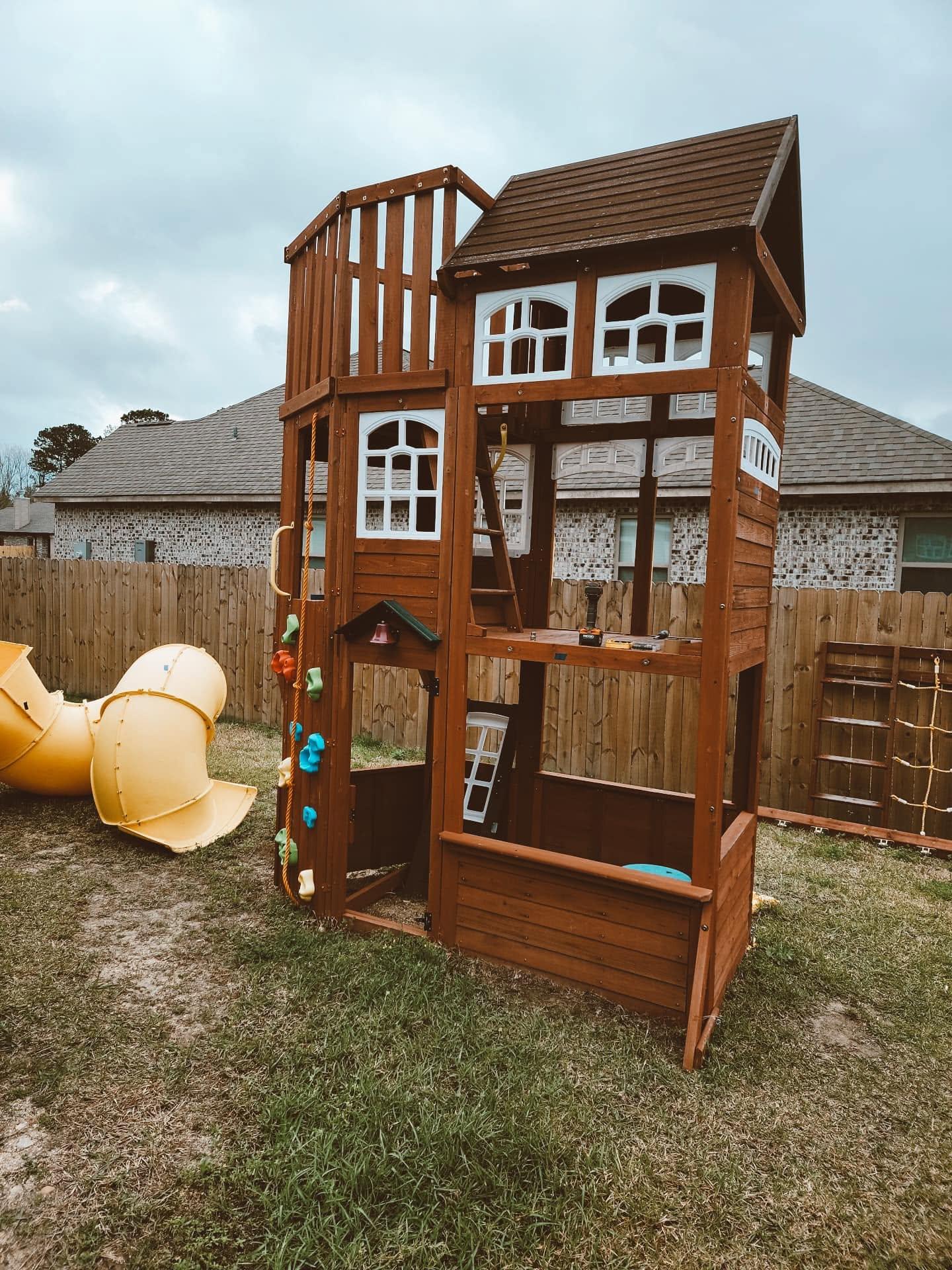 An assembled wooden playset with a slide and climbing wall